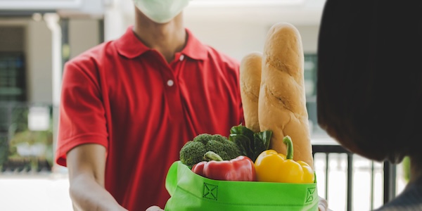 food delivery service man with protection face mask in red uniform holding fresh food